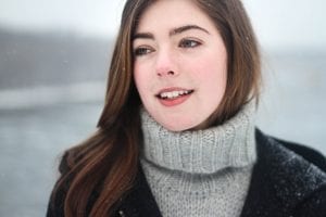 a woman in a wintry scene, snowflakes on her hair and coat, with clear skin